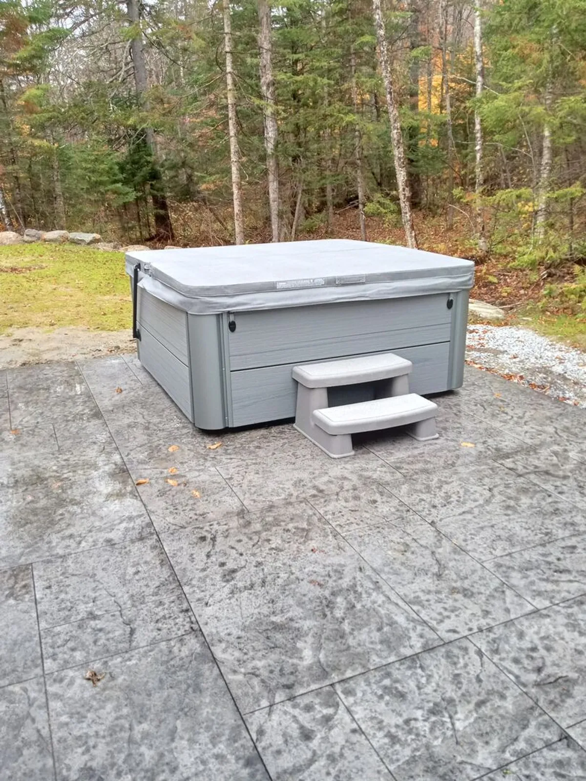 This exterior shot highlights a peaceful patio scene featuring a hot tub, surrounded by trees and a smooth patio surface. The setting is serene, perfect for socializing or enjoying a quiet moment outdoors, especially after a day of winter sports.