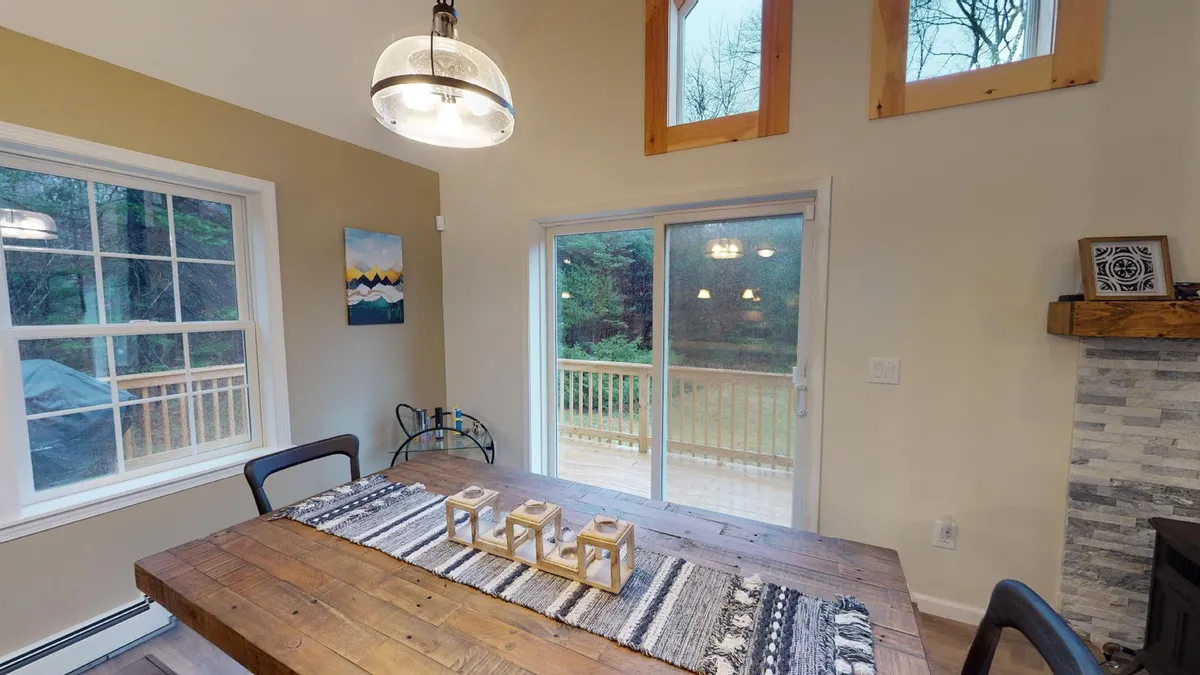 A cozy dining area featuring a wooden table, large windows with views, a decorative centerpiece, and a stone fireplace. The natural light and views outside connect the space to the surrounding environment, while the setting invites family meals and game nights.