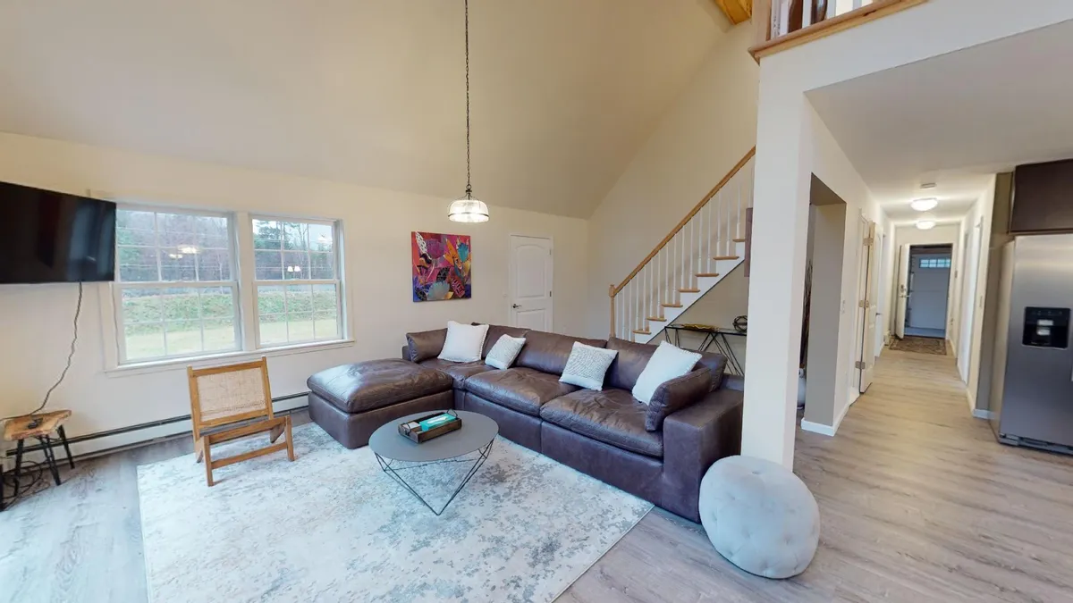 A spacious living room with a large sectional sofa, contemporary artwork, a coffee table, and windows with views to the outdoors. The setting is perfect for socializing, watching movies, or enjoying quiet moments together.
