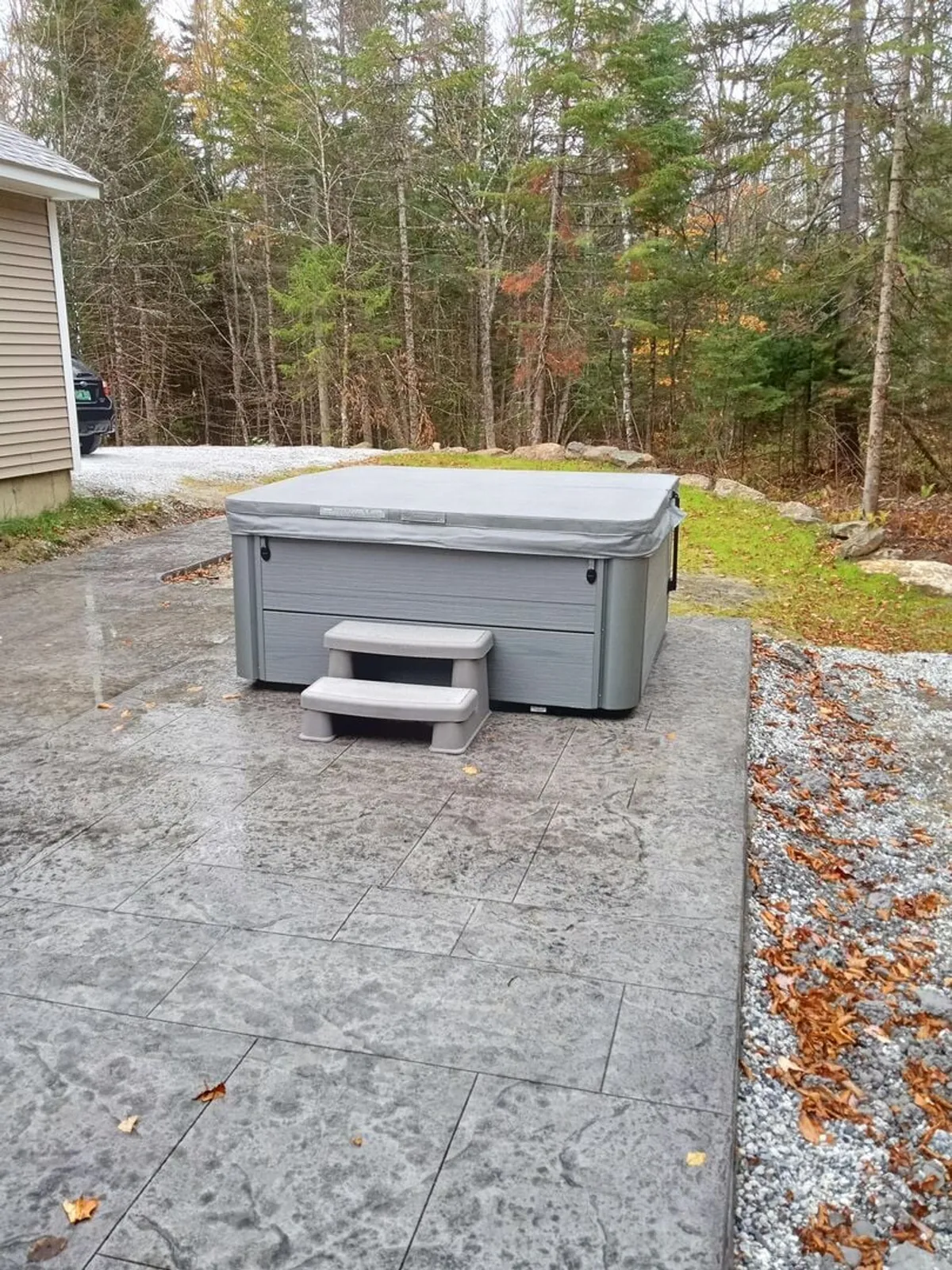 This exterior image showcases a private hot tub nestled amid surrounding trees on a paved patio. The tranquil outdoor setting is perfect for relaxing after a day on the slopes, with plenty of space for socializing or enjoying nature under the open sky.