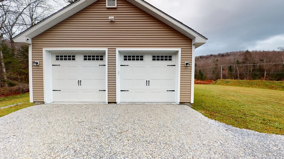 An inviting exterior view with garage doors, a gravel driveway, and lush surrounding greenery. This scene conveys easy access for guests traveling with gear or vehicles, while the green setting suggests a peaceful, nature-oriented retreat close to major ski areas.