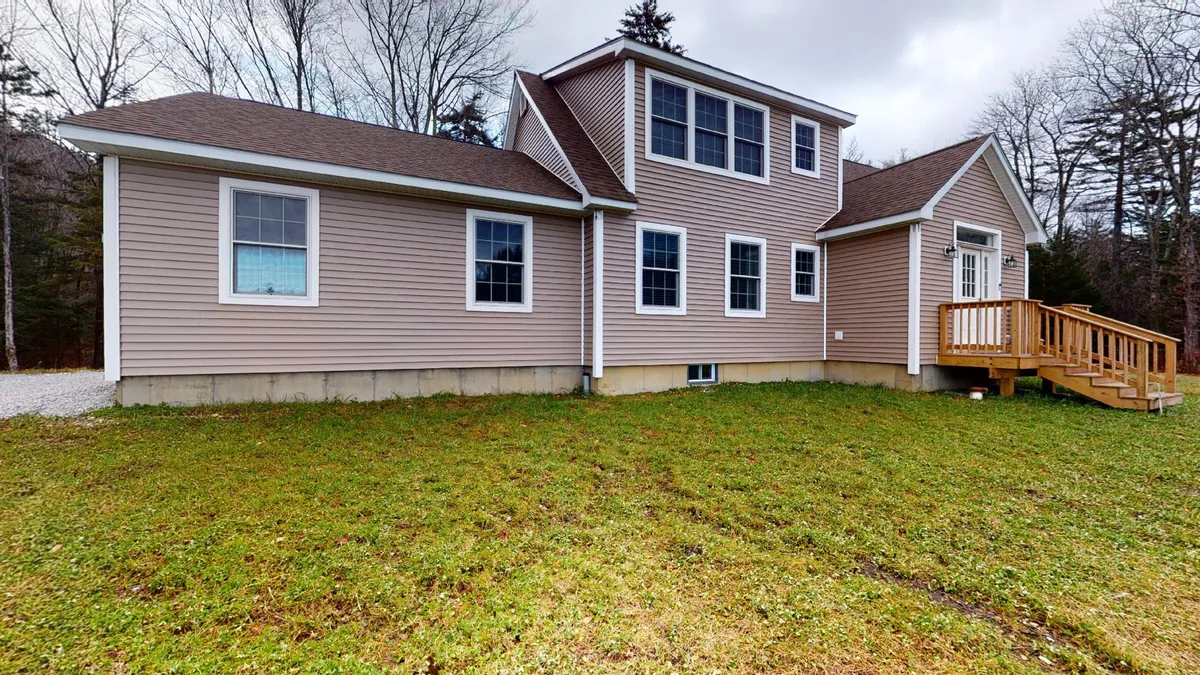 A wide view of the property's wooden deck set against a backdrop of large windows and an asymmetrical roofline. The scene is filled with natural light and hints at spacious outdoor living, as the deck overlooks peaceful greenery, inviting guests to relax or host gatherings in nature.